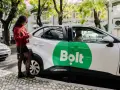 Junge Frau öffnet Tür eines weißen Bolt-Taxis. Fahrer wartet.