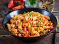 Penne w pikantnym sosie pomidorowym z kawałkami kurczaka, groszkiem i świeżymi ziołami. Danie wygląda jak pyszne spaghetti arrabiata.