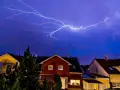 Błyskawica przecina fioletowe niebo nad domami. Dobry uziemienie domu chroni przed burzą.