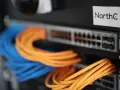 Netzwerkschrank mit blauen und orangen Kabeln, die an einen Switch angeschlossen sind.