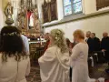 Uroczystość w kościele. Kobieta w białej sukni, z kwiatami we włosach, klęczy. To moment konsekracji, ważny dla dziewicy konsekrowanej.
