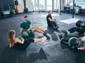 Fünf Personen machen im Fitnessstudio Sit-ups mit Medizinbällen.