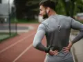 Uomo con le mani sulla schiena, che indica dolore. Forse correre fa male alla schiena, o forse è solo un momento di pausa.
