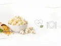 Miseczka popcornu, obok łopatka z ziarnami kukurydzy. Czy popcorn jest lekkostrawny? Ikony serca i talerza sugerują zdrowy posiłek.