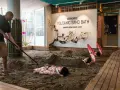 A man rakes sand for a volcanic sand bath. Two people lie buried in the sand, with red umbrellas over their heads.