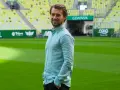 Uśmiechnięty Tomasz Kaczmarek, trener, stoi na tle stadionu w Gdańsku.