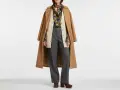 Modello con cappotto cammello, cardigan beige, camicia fantasia, pantaloni grigi e scarpe marroni. Un esempio di vestirsi a cipolla significato per adattarsi a ogni temperatura.