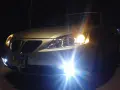 Srebrny samochód nocą, włączone światła przeciwmgielne i reflektory rozświetlają drogę.