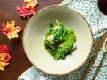 Piatto di carne con salsa verde cremosa, guarnito con cime di rapa fresche. Accanto, foglie autunnali e posate dorate.