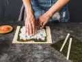 Ręce rozkładają ryż na nori, przygotowując się do zwijania sushi. To kluczowy krok, jak ugotować ryż do sushi.