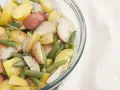 Insalata colorata di fagiolini e patate novelle, condita con erbe aromatiche, in una ciotola di vetro.