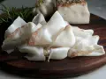 Fette sottili di lardo di Colonnata, profumate con rosmarino e aglio, pronte per essere gustate.