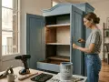 Mujer restaurando muebles antiguos, pintando un armario azul con detalles de papel tapiz. Herramientas y pintura a la vista.