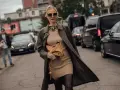 Une femme élégante porte un trench-coat kaki sur une robe moulante beige, un sac Fendi et des bottes hautes. Parfait pour savoir quoi mettre par-dessus une robe de soirée.