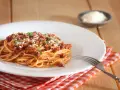 Talerz spaghetti bolognese z parmezanem i natką pietruszki, obok widelec i ser w miseczce.