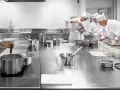 Estudiantes de cocina aprenden sobre seguridad en la cocina, preparando ingredientes en una estación de acero inoxidable.