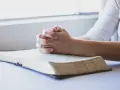 Dłonie złożone w modlitwie nad otwartą księgą, symbolizujące modlitwę przed nauką.