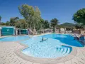 Dzieci pluskają się w basenie na terenie Miramare Camping Village. Słoneczny dzień, błękitne niebo i zieleń drzew tworzą wakacyjny klimat.