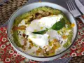 Un bol de purée verte, peut-être une sauce petit pois, garni d'un œuf poché, de crème, d'amandes effilées et d'une feuille de basilic.