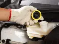 Ręka w rękawiczce trzyma żółtą zakrętkę od zbiorniczka płynu sprzęgła.