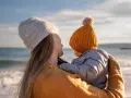 Madre abraza a su bebé en la playa, disfrutando de un momento de paz. Un respiro merecido, como una excedencia y vacaciones no disfrutadas, antes de volver a la rutina.
