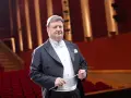 Jacek Boniecki, dyrygent w eleganckim fraku, z batutą w dłoni, na tle czerwonej widowni. Jego życiorys to historia pasji do muzyki.