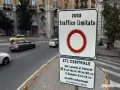 Cartello che indica "zona traffico limitato" con orari specifici. Auto in transito su strada urbana.