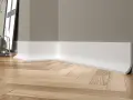 Białe listwy przypodłogowe kontrastują z drewnianą podłogą, tworząc eleganckie wykończenie.