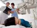 Lekarz i technik elektroradiolog omawiają badanie RTG pacjentki leżącej na stole.
