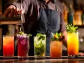 Barman przelewa drinka z shakera. Na blacie stoi rząd kolorowych koktajli, każdy ozdobiony owocami i miętą. Idealny przykład, jak zrobić dobry drink.