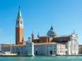 Il campanile di Venezia si erge maestoso accanto alla chiesa con la cupola, mentre barche a vela attendono sul canale.