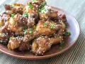 Alitas de pollo glaseadas con sésamo y cebolleta en un plato marrón.
