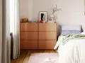Moderne schlafzimmer ideen: Orange Kommoden neben einem Bett mit gestreifter Kissen und grüner Decke. Ein rosa Teppich und Hausschuhe liegen auf dem Holzboden.