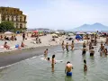 Gente che si gode il sole e il mare sulle spiagge libere di Napoli, con il Vesuvio sullo sfondo.