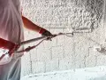 Pracownik w rękawicach nakłada tynk cementowy na ścianę za pomocą agregatu. Kluczowe są tu szpryc cementowy proporcje, by uzyskać idealną konsystencję.