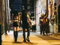 Dwie osoby w stylach gotyckich ubraniach idą wąską uliczką nocą.