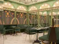 Elegante restaurante con mesas y sillas verdes, paredes decoradas con girasoles y detalles dorados. Un lugar perfecto para disfrutar de **frases restaurante** inspiradoras.