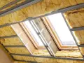 Ocieplenie poddasza z wełny mineralnej w trakcie montażu. Widoczne okna dachowe i metalowe profile konstrukcyjne.