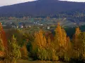 Jesienny krajobraz z kolorowymi drzewami i domami w dolinie. W tle widać łagodne **góry świętokrzyskie szczyty** porośnięte lasem.
