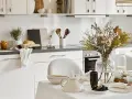 Cuisine lumineuse dans une maison style cottage anglais, avec vaisselle et bouquet de fleurs séchées sur la table.