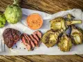 Saftiges Steak und gegrillte Artischocken mit Dip auf Holzuntergrund.