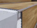 Zbliżenie na schody z paneli drewnianych, z widocznym profilem aluminiowym i warstwą izolacyjną.
