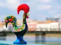 Un gallo de cerámica negro, decorado con flores y corazones, se alza orgulloso con su cresta roja.