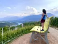 Donna ammira il panorama da una panchina gialla gigante, circondata da vigneti e montagne.