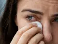 Occhi lacrimosi: una donna si asciuga le lacrime con un fazzoletto. Le cause possono essere molteplici, dal dolore alla stanchezza.