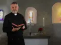 Ein Mann mit grauem Bart und Priesterkragen hält ein Buch in einer Kirche. Er hat sich entschieden, Priester zu werden.