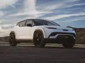 Biały SUV Fisker z czarnym dachem i przyciemnianymi szybami, zaparkowany na drodze z widokiem na wzgórza i niebo.