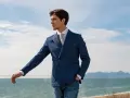 Uomo con giacca doppiopetto blu a righe, camicia bianca e cravatta, jeans. Eleganza classica uomo con vista mare.