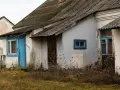 Stary dom z niebieskimi drzwiami i oknami, zarośnięty chwastami. Budowa domu w granicy działki wymaga zgody sąsiada.