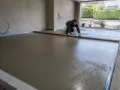 Pracownik wyrównuje świeżą wylewkę betonową na zewnątrz, przygotowując podjazd.